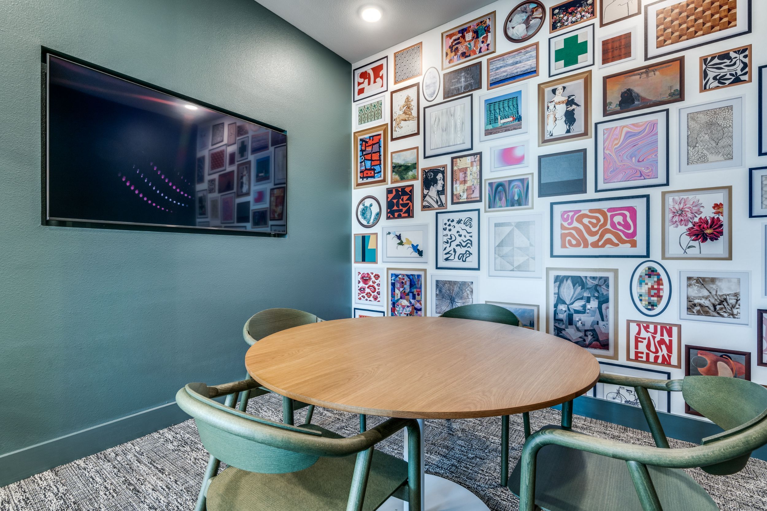 A modern meeting room with a round table and a wall of framed artworks