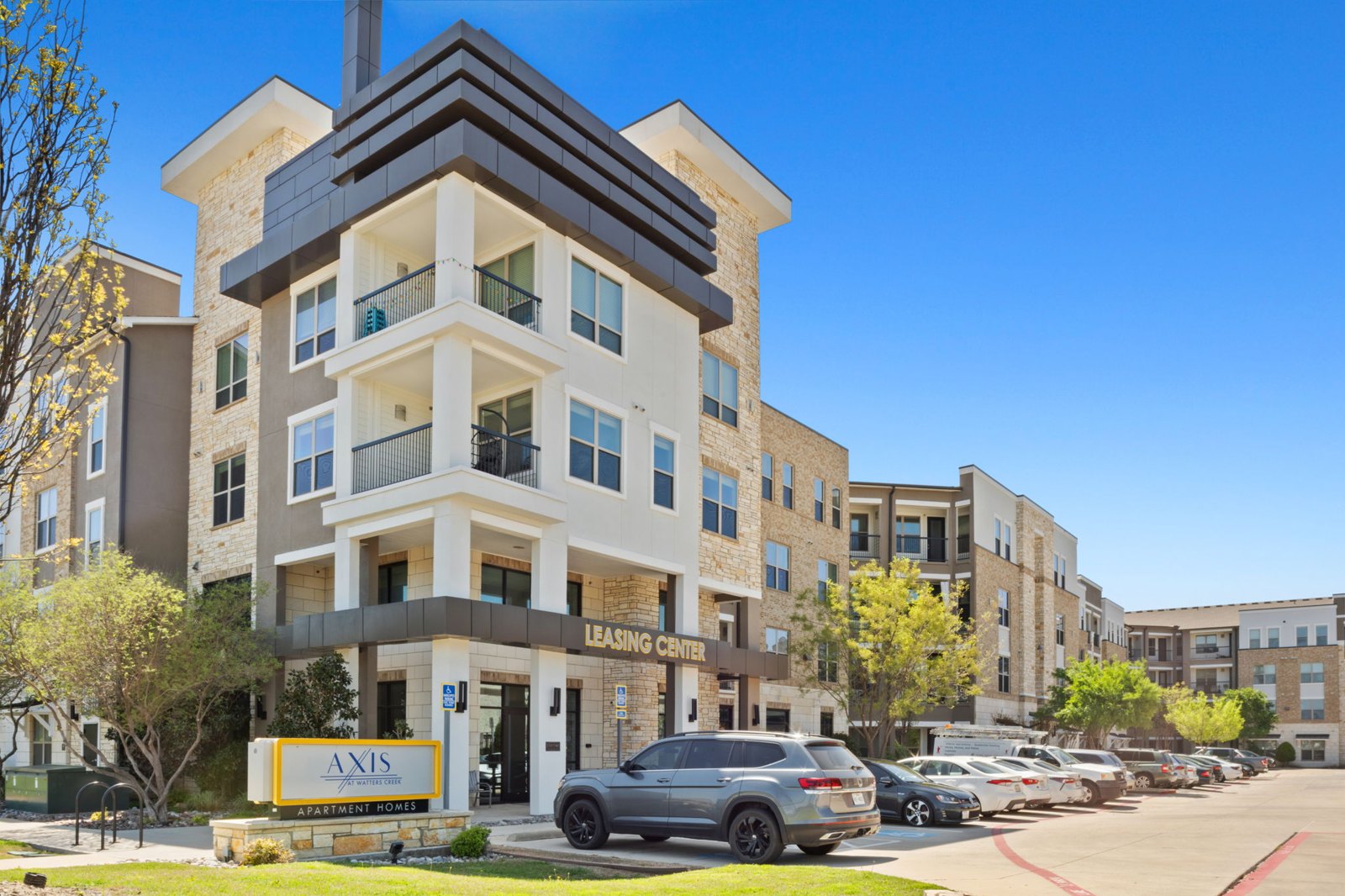 A modern apartment building with a leasing sign in front. at Axis at Watters Creek