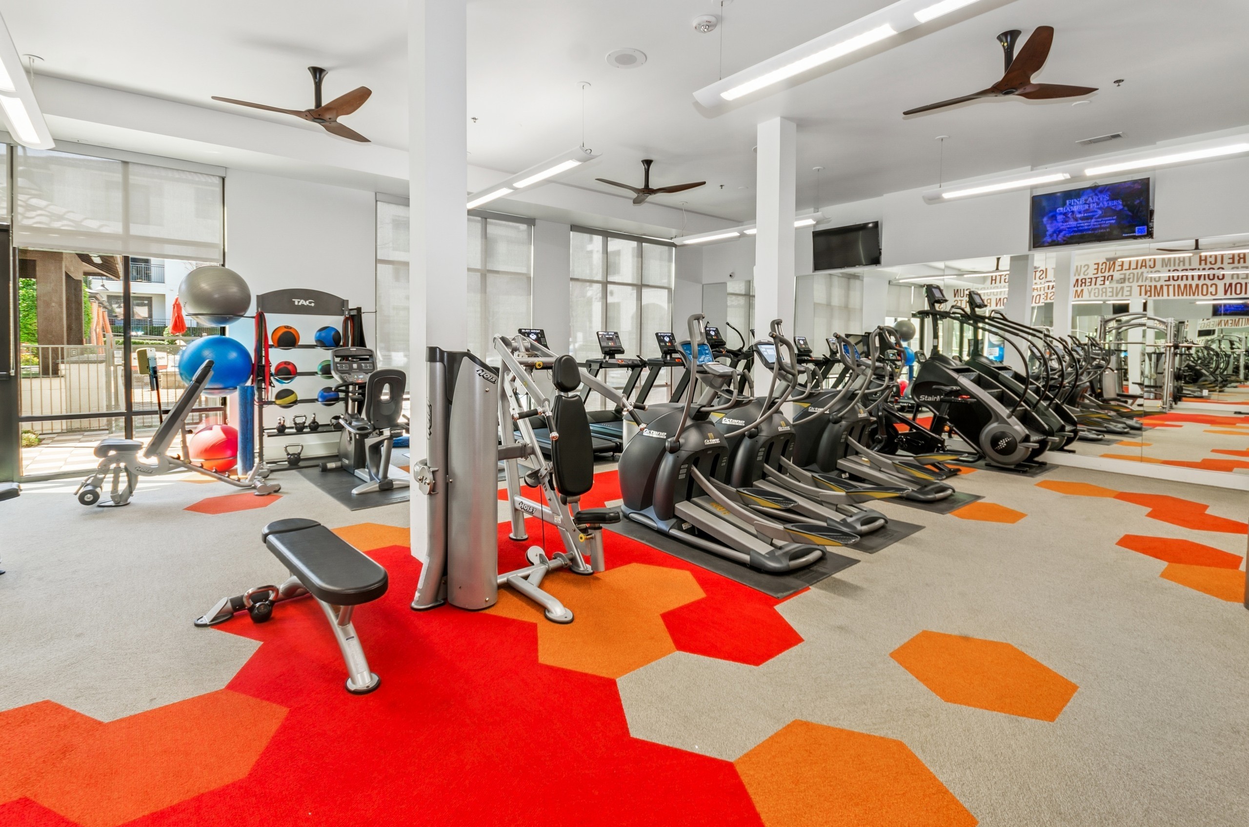 Modern gym at AMLI on Riverside with treadmills, ellipticals, and weight machines with a bright red and orange hexagonal patterned floor
