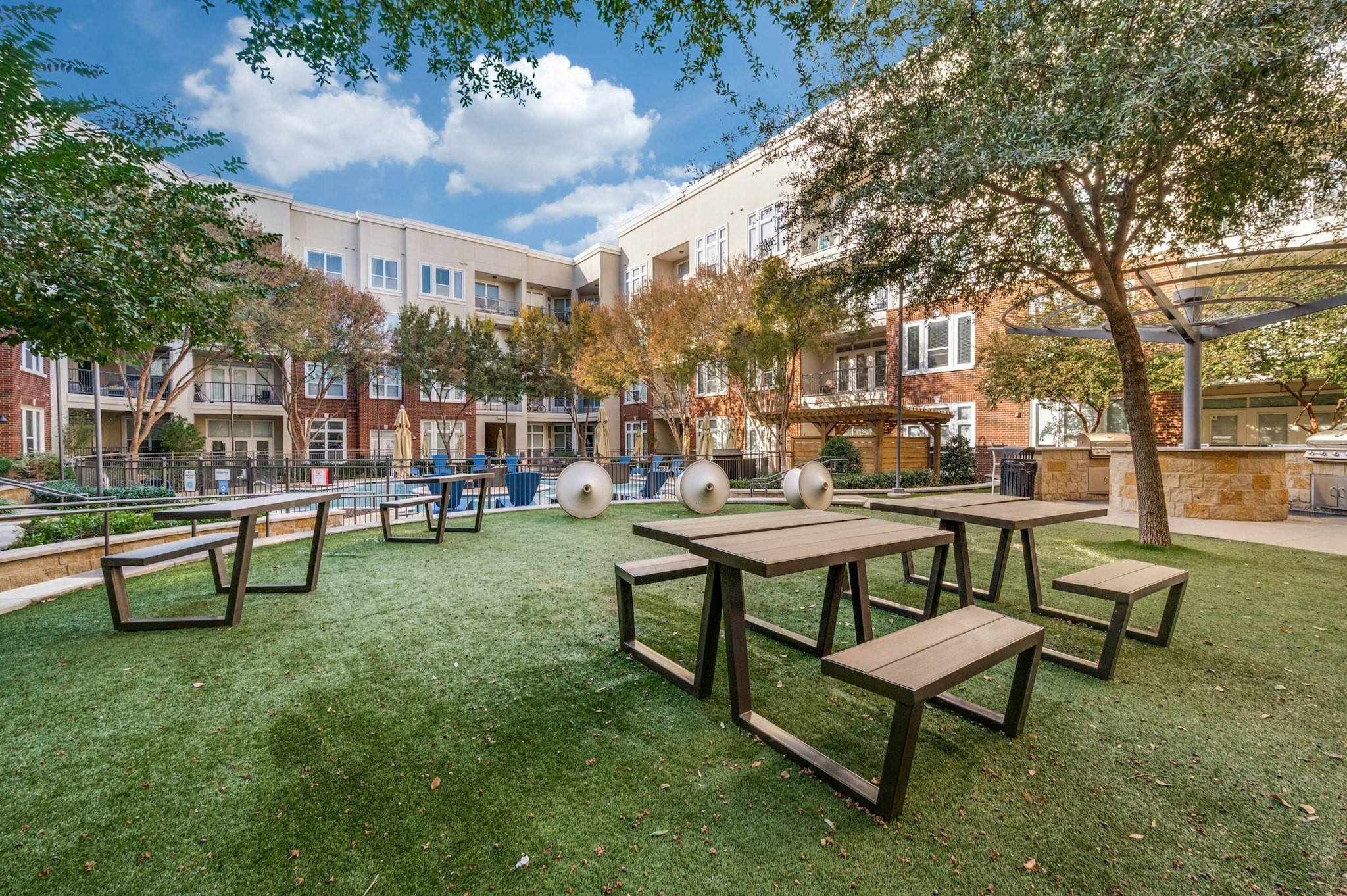 AMLI Frisco Crossing - Outdoor courtyard lawn with picnic tables, sculptural seating, and barbecue grills overlooking the pool at AMLI Frisco Crossing apartments