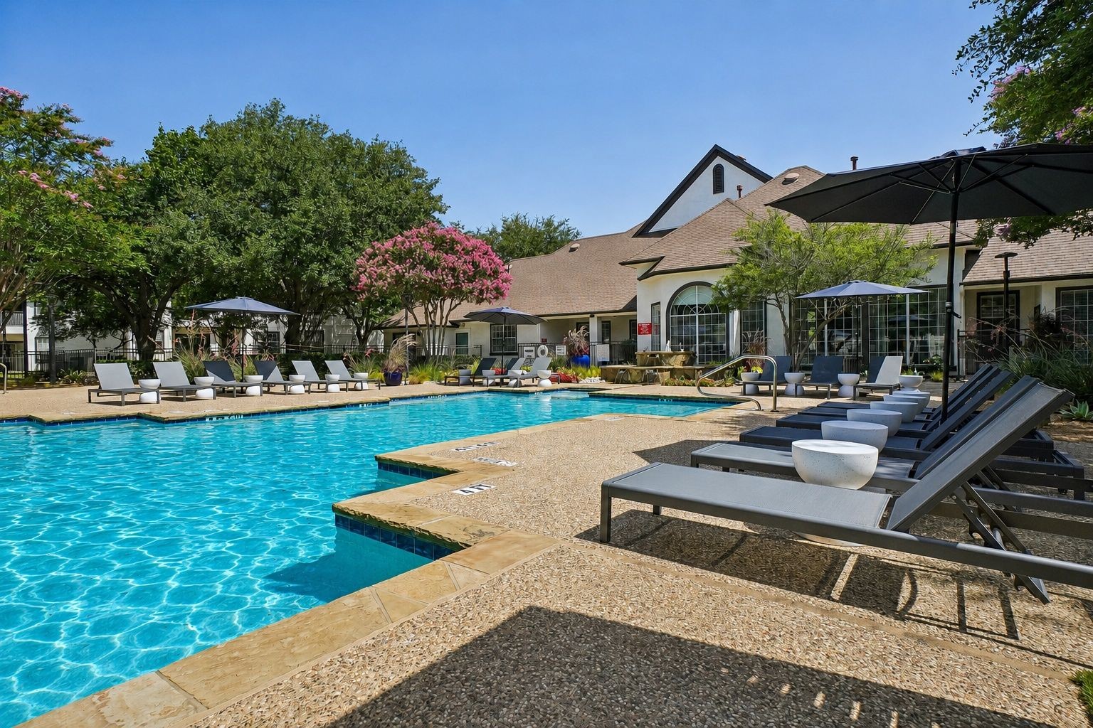 23Hundred at Ridgeview - A sunny pool area with lounge chairs and umbrellas, surrounded by greenery