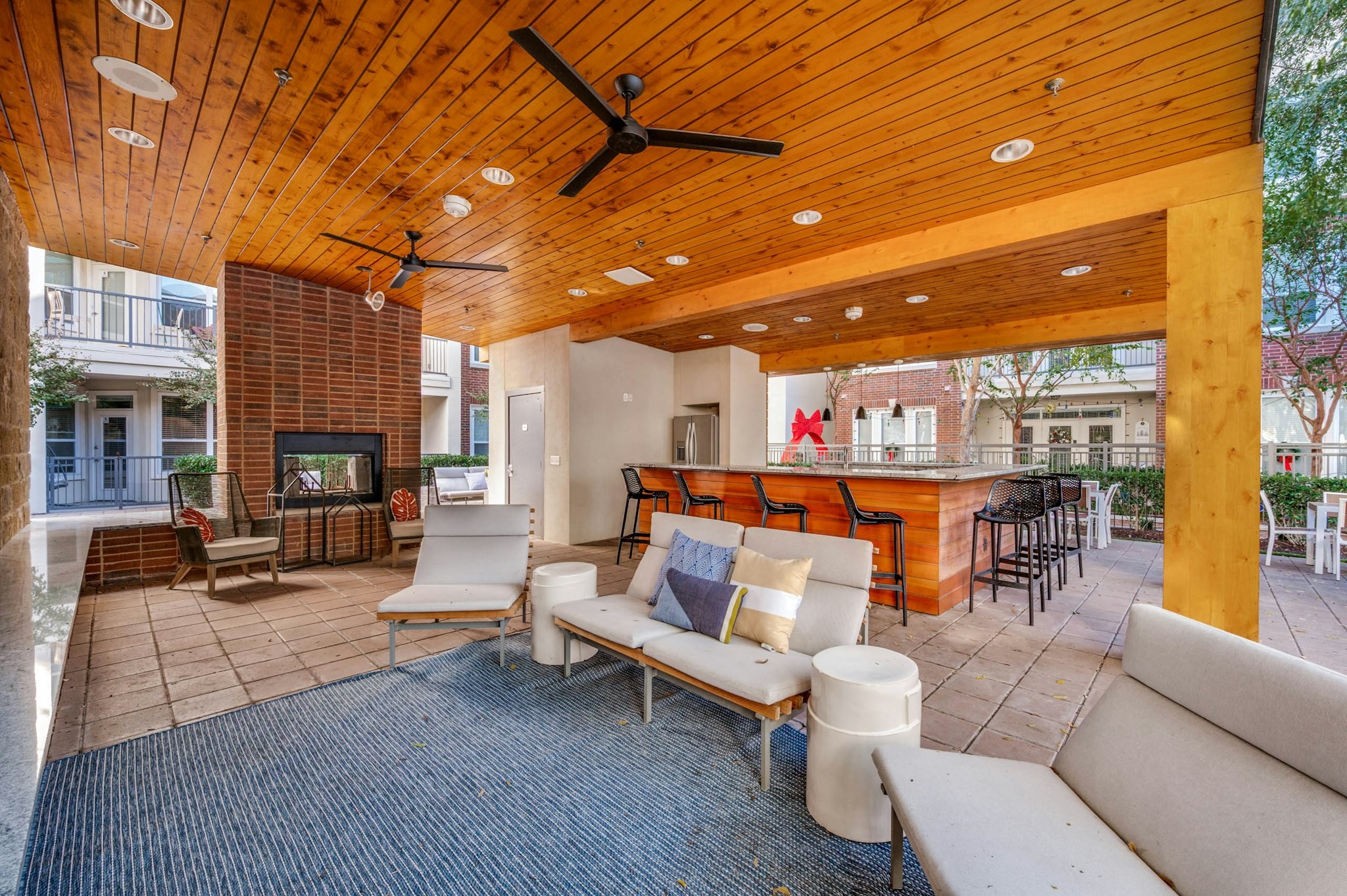 AMLI Frisco Crossing - Shaded outdoor lounge area with ceiling fans, cushioned seating, brick fireplace, and bar at AMLI Frisco Crossing apartments
