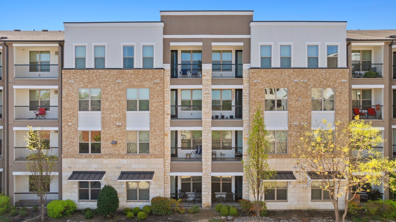 A row of apartment buildings with balconies and trees in front. at Axis at Watters Creek