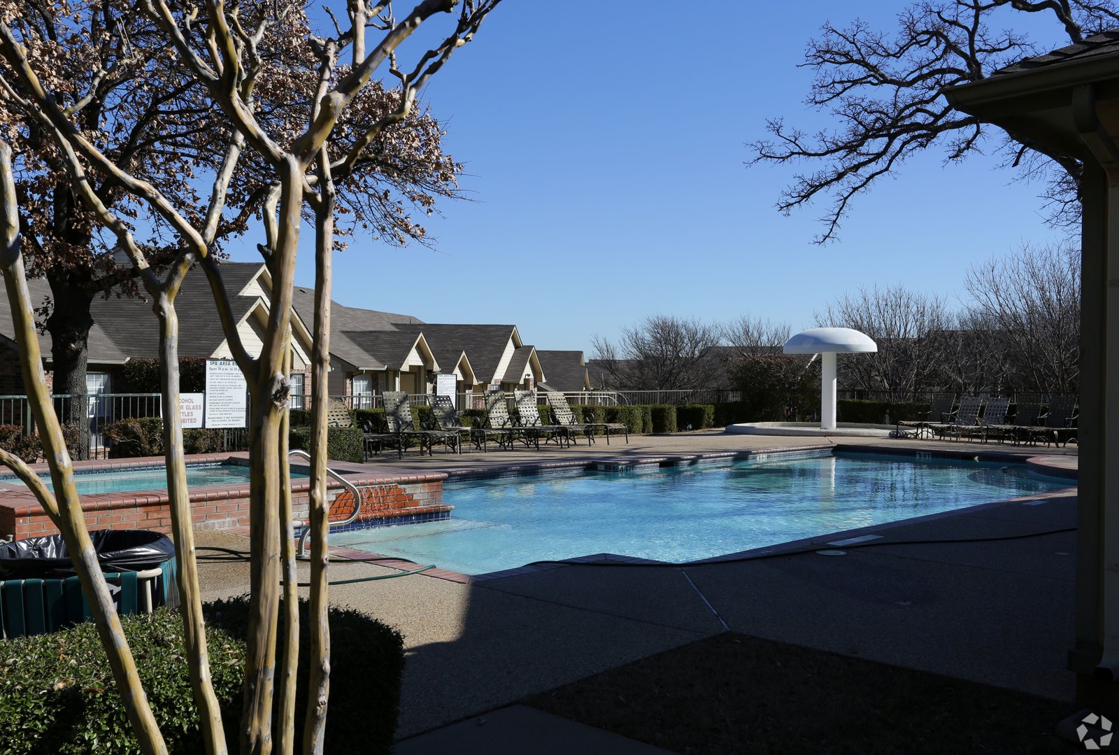 A pool surrounded by trees and a building in the background. at Ash Lane Apartment Homes