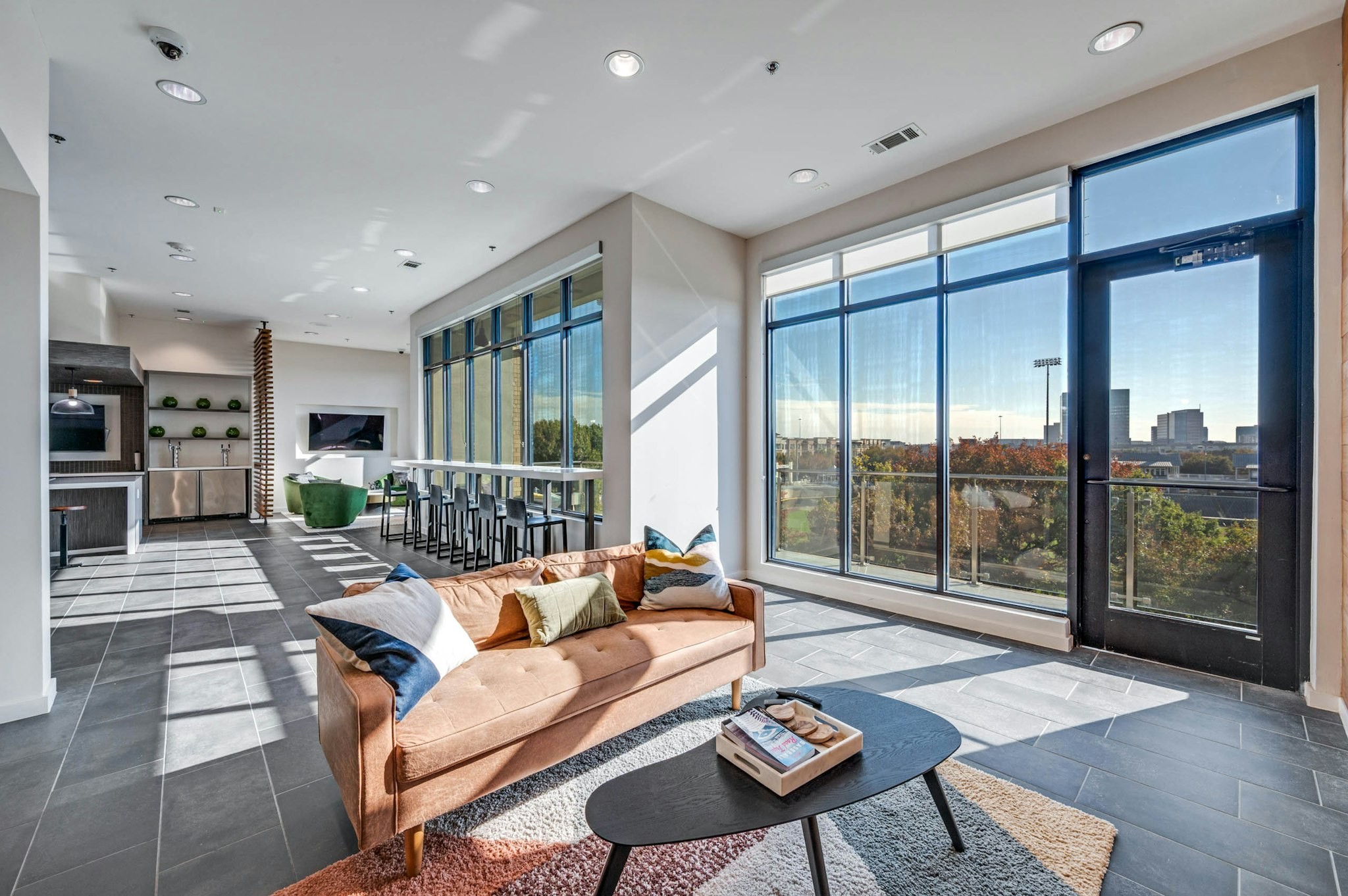 AMLI Frisco Crossing - Spacious lounge area with large windows, bar seating, plush tan sofa over a decorative rug at AMLI Frisco Crossing apartment sky lounge
