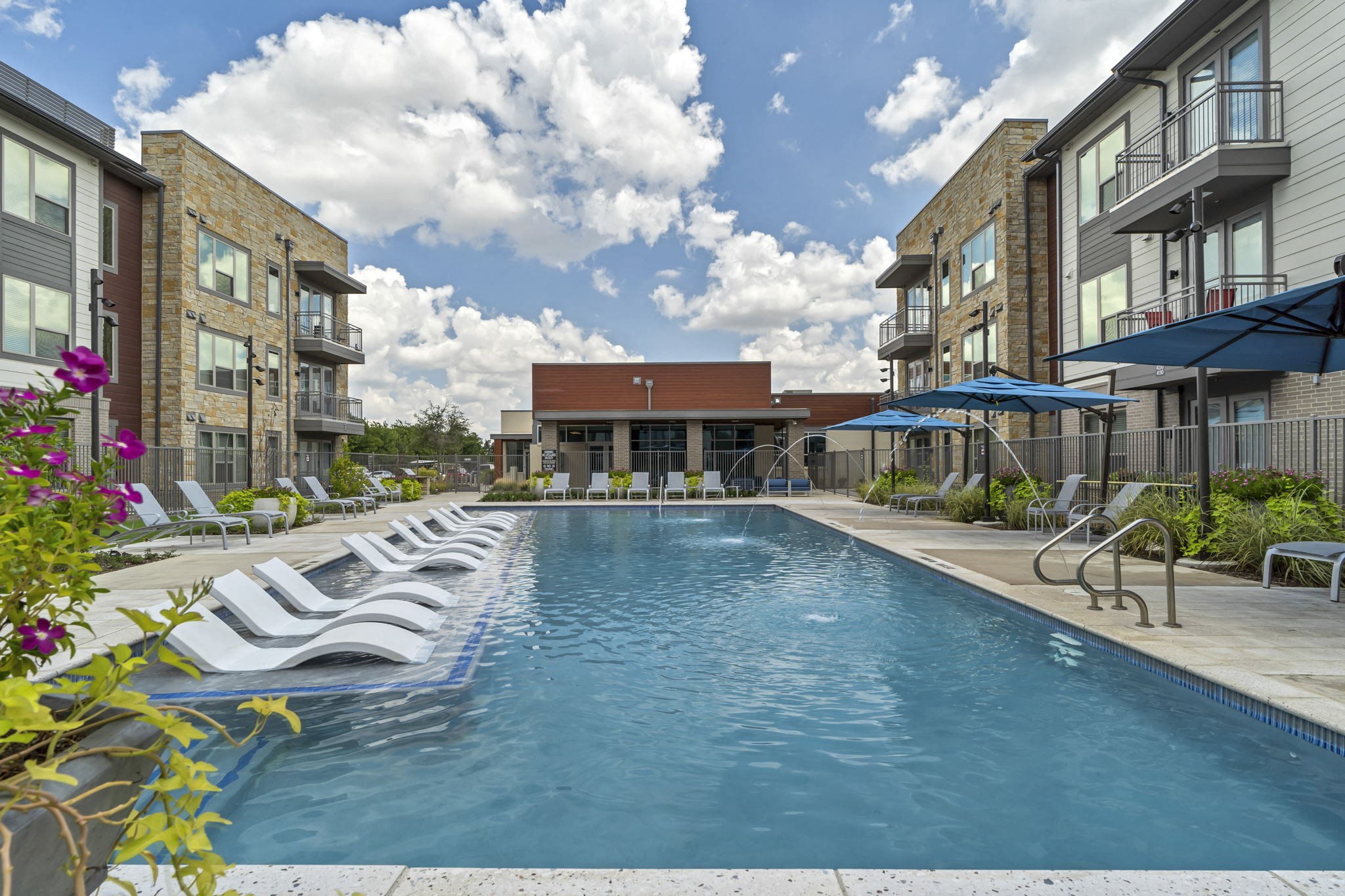 26 at City Point - A swimming pool surrounded by lounge chairs and umbrellas in front of apartment buildings