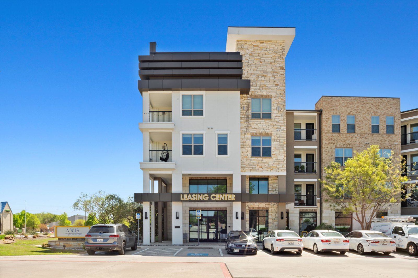 A modern building with a leasing center sign in front. at Axis at Watters Creek