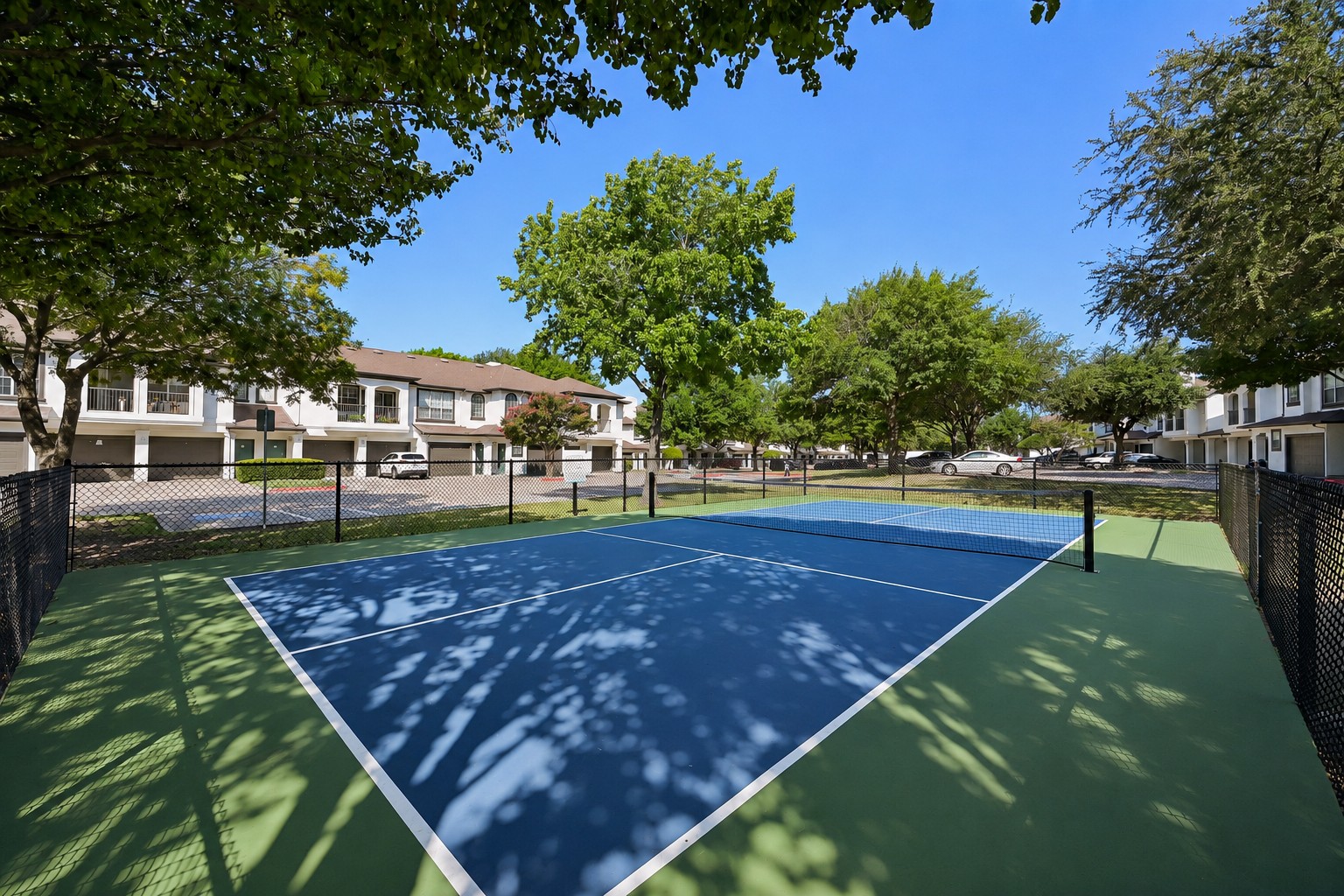 23Hundred at Ridgeview - Empty tennis court surrounded by trees and residential buildings on a sunny day
