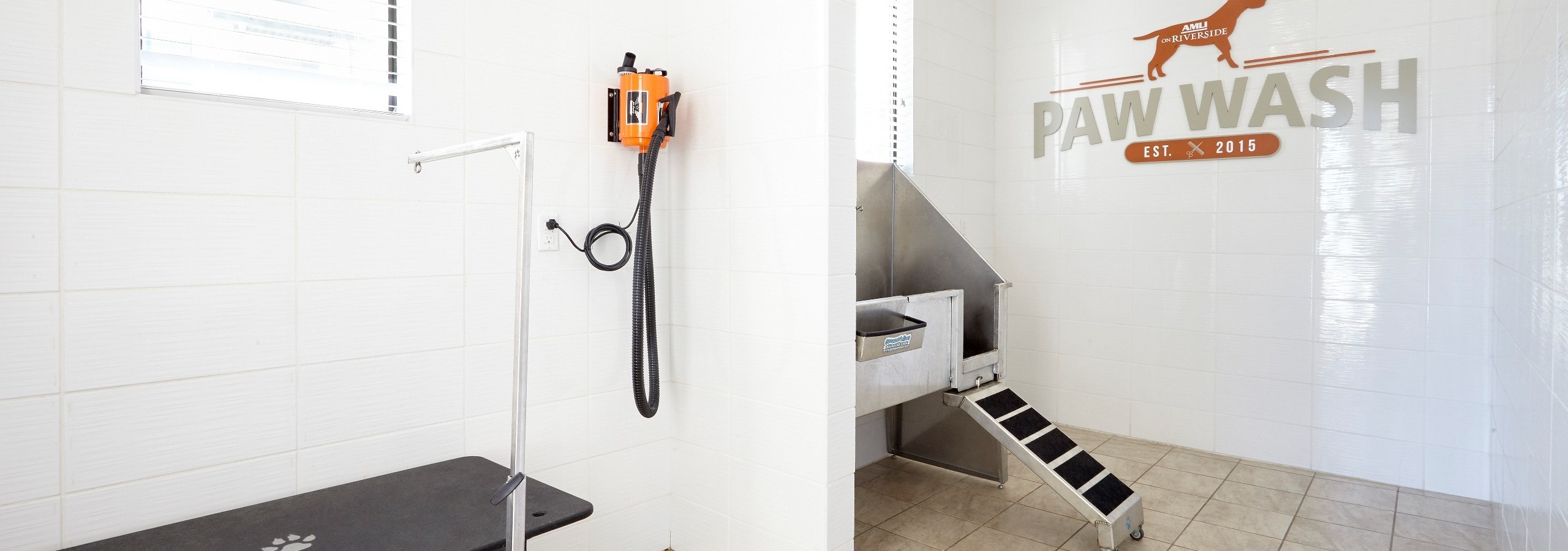 Paw wash at AMLI on Riverside with beige tiled floors and white tiled walls with a stainless steel tub and a table to dry off