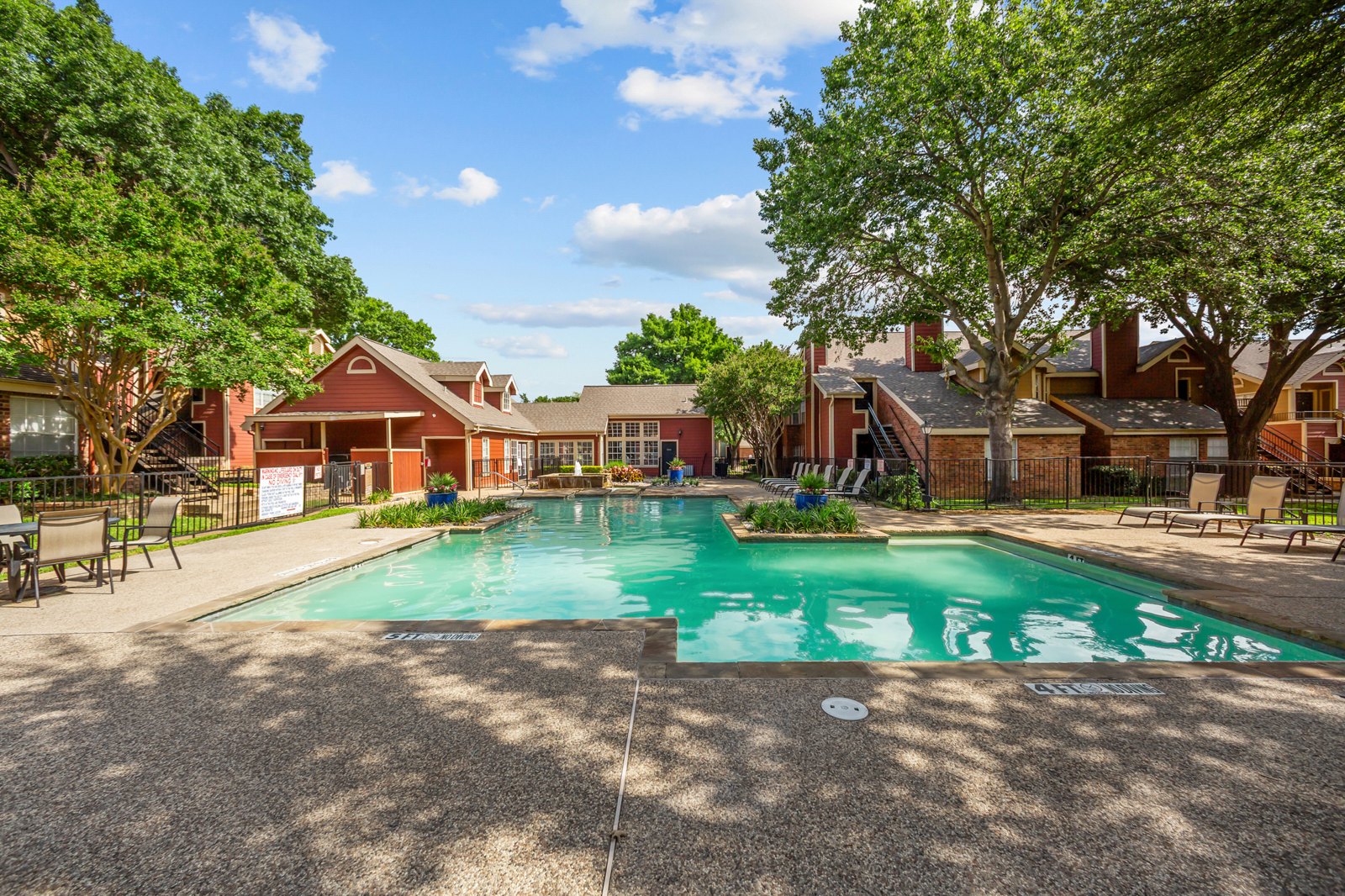 A large swimming pool surrounded by trees and a building in the background. at Bravo Apartment Living