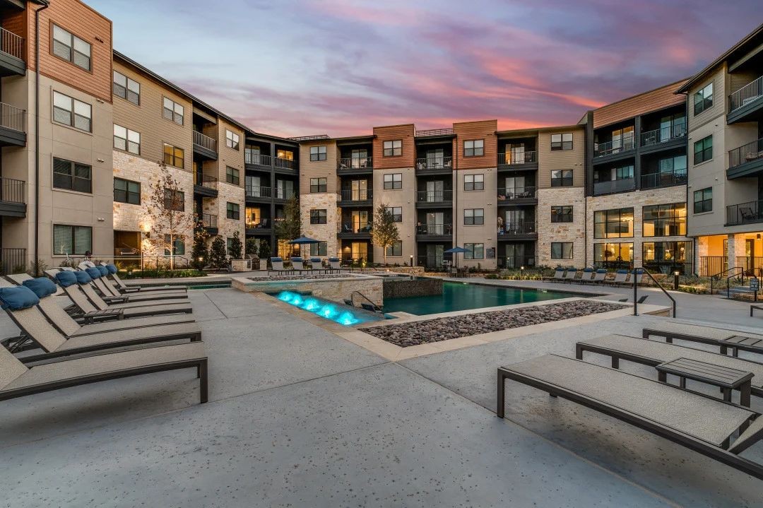 a swimming pool with chaise lounge chairs in front of an apartment building