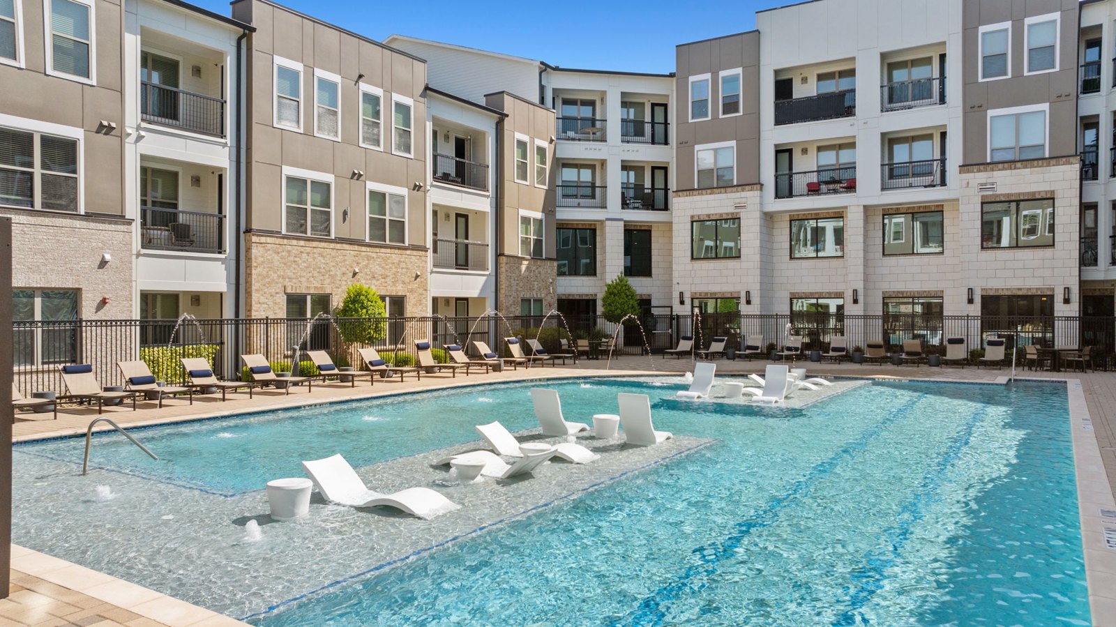 A large swimming pool with lounge chairs in front of apartment buildings. at Axis at Watters Creek