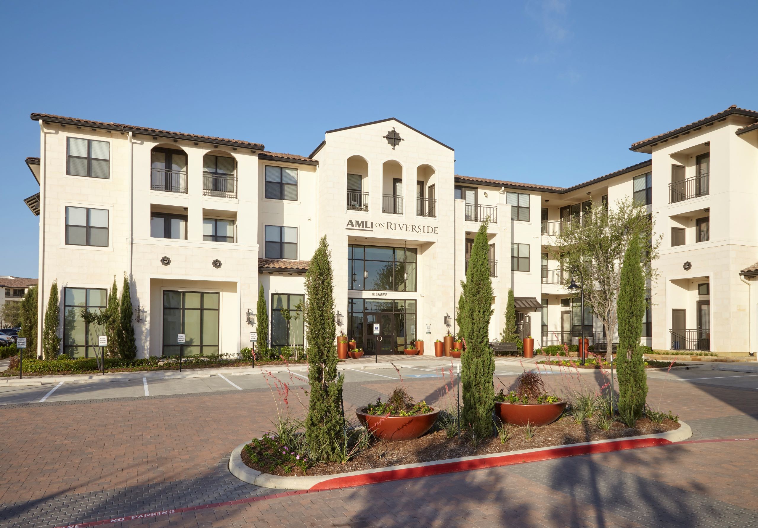 Exterior of AMLI on Riverside building with white stucco facade with logo above door and surrounding trees and bushes