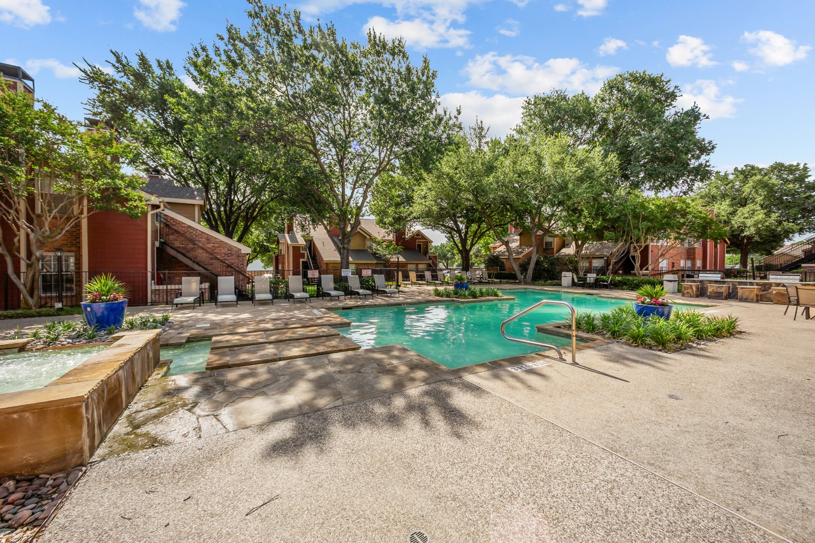 A pool surrounded by trees and a building in the background. at Bravo Apartment Living