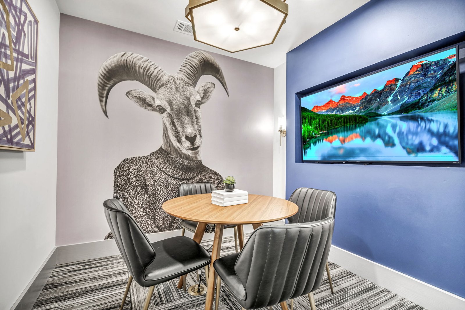 A room with a table, chairs, and a large screen displaying a mountain landscape. at Axis Grand Crossing