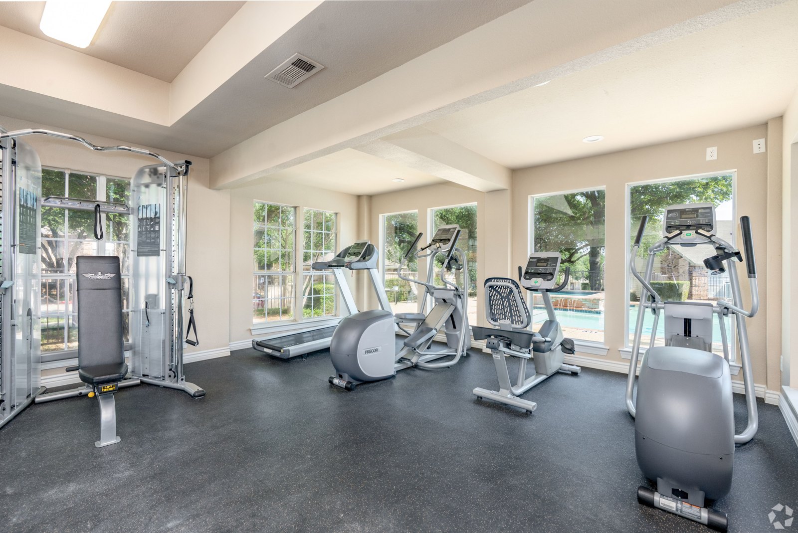 A spacious gym with a variety of equipment including treadmills, elliptical machines, and a weight machine. at Ash Lane Apartment Homes
