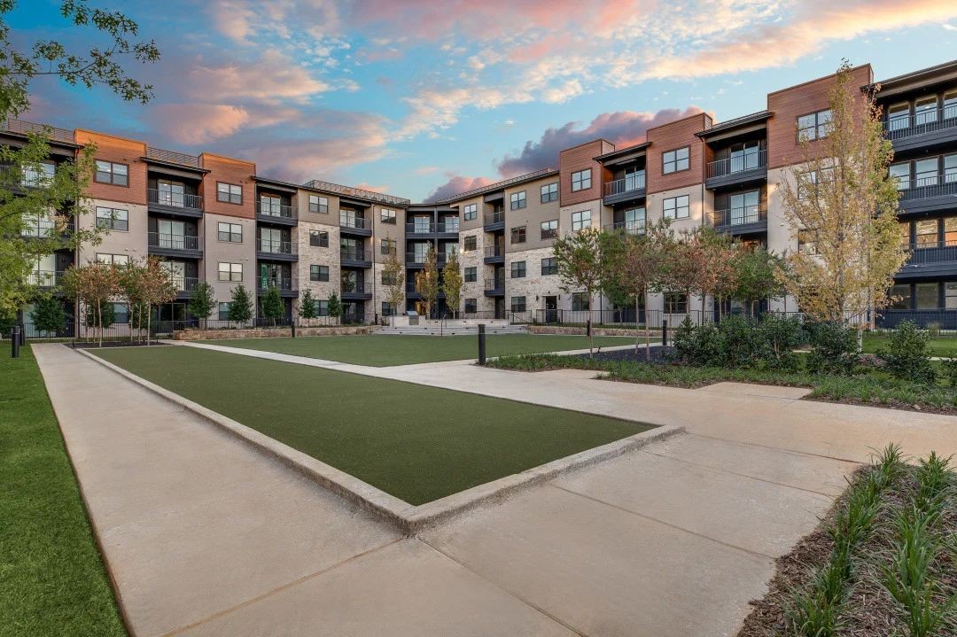 a courtyard with a grassy area and apartment buildings in the background