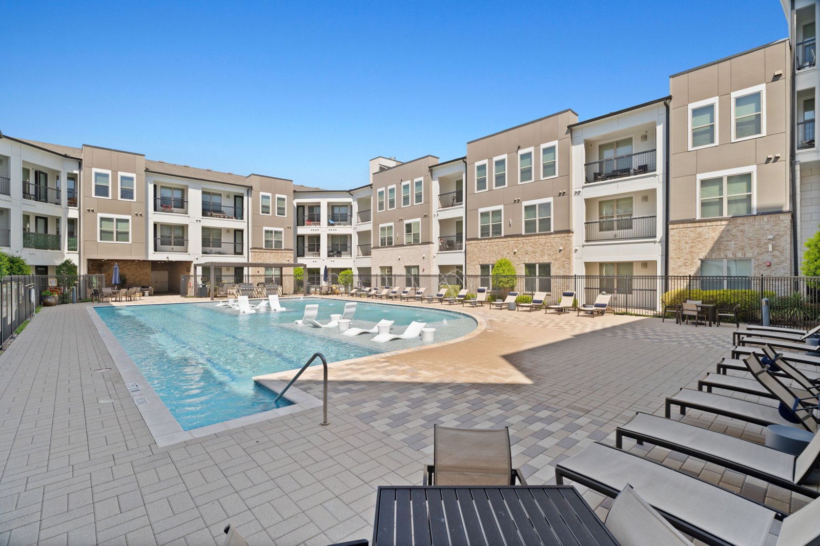 A swimming pool surrounded by apartment buildings and lounge chairs. at Axis at Watters Creek