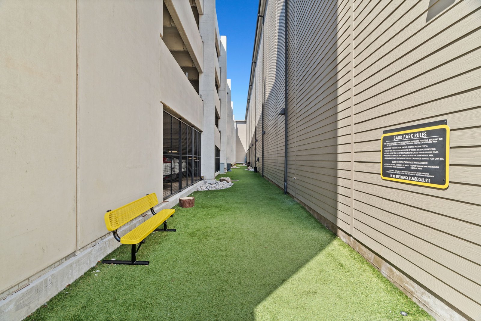 A yellow bench sits on a green lawn next to a building. at Axis at Watters Creek