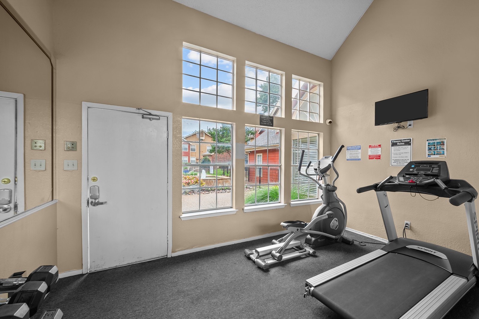 A gym room with a treadmill, exercise bike, and other equipment. at Bravo Apartment Living