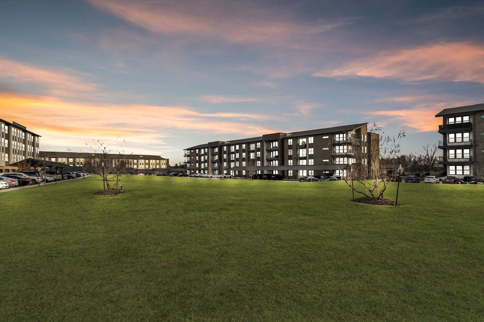 A large grassy field in front of a building with a sunset in the background. at Axis Grand Crossing