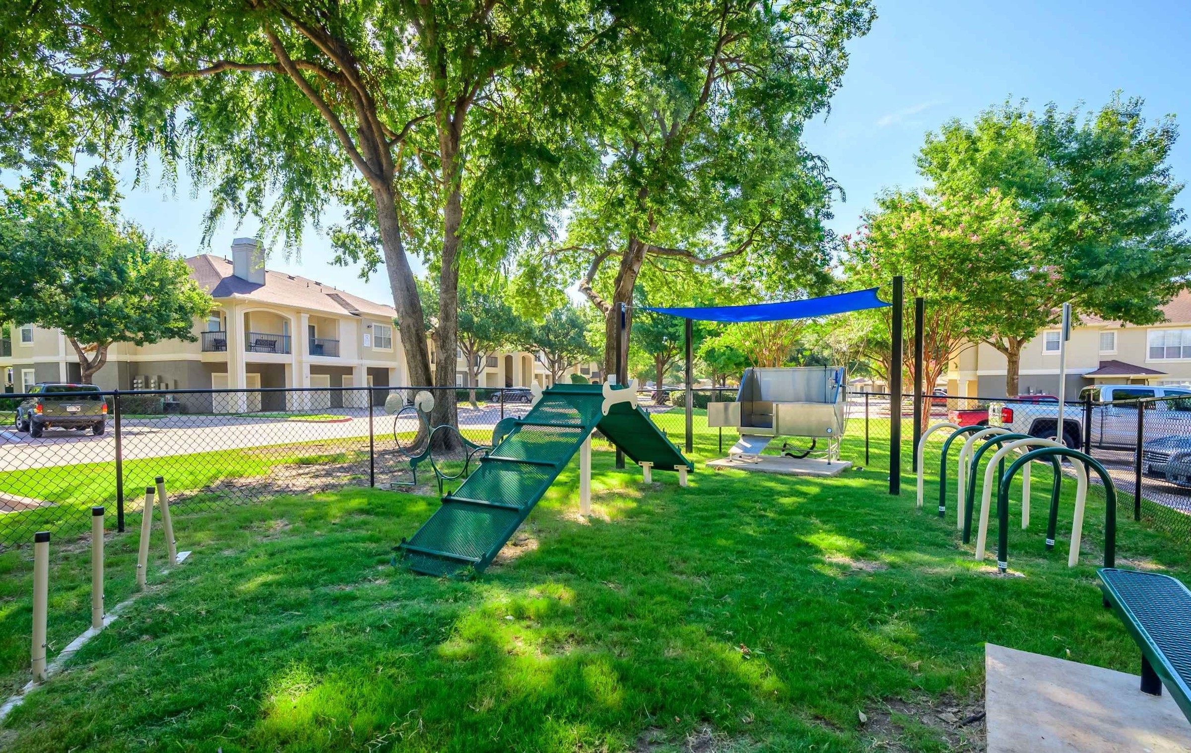23Hundred at Ridgeview - A playground area with slides, a climbing structure, and shaded seating surrounded by green grass