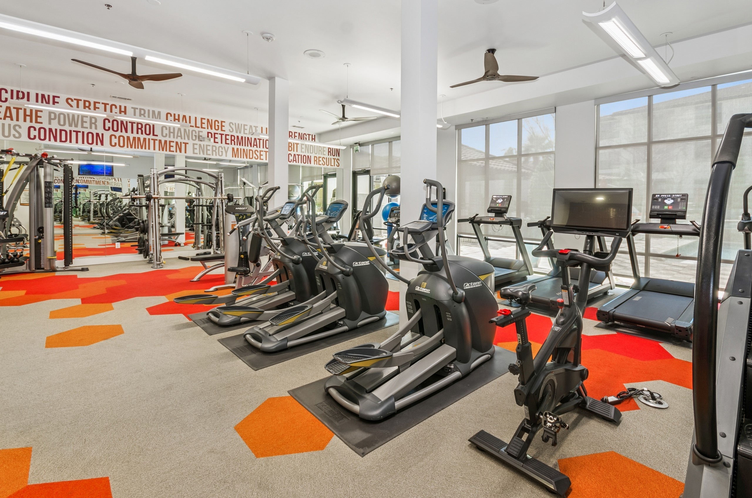 Exercise equipment at the AMLI on Riverside fitness center with geometric pattern flooring, and motivational words on the walls