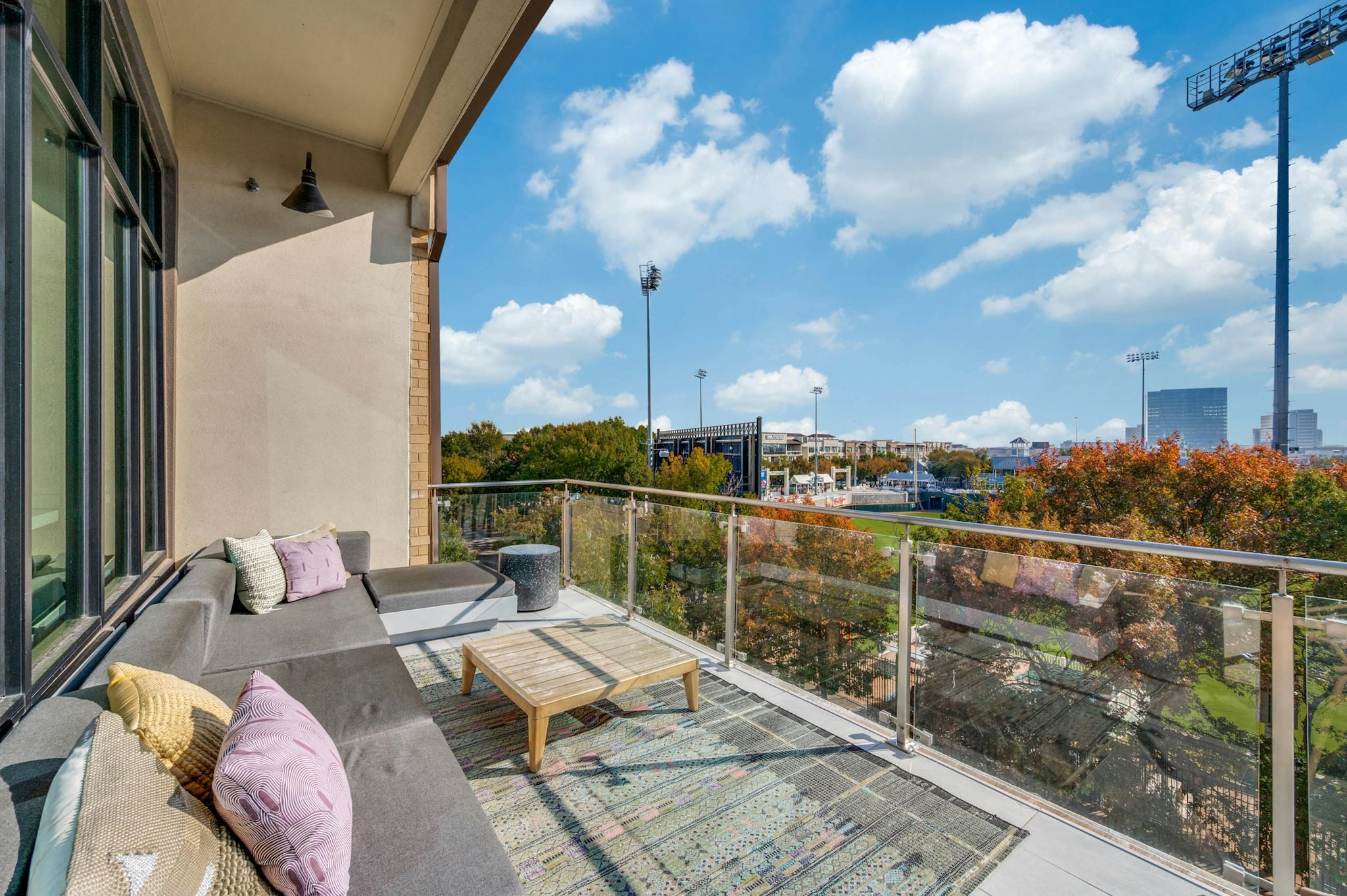 AMLI Frisco Crossing - Balcony lounge area with plush sectional sofa, throw pillows, coffee table, and stadium views at AMLI Frisco Crossing apartments