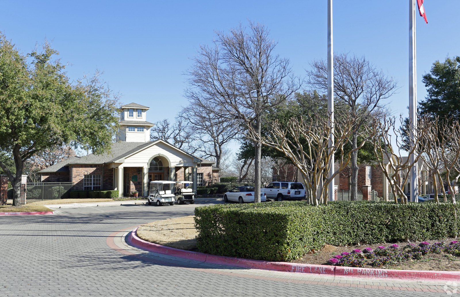 A building with a tower and a flag on top is surrounded by trees and has a driveway leading to it. at Ash Lane Apartment Homes