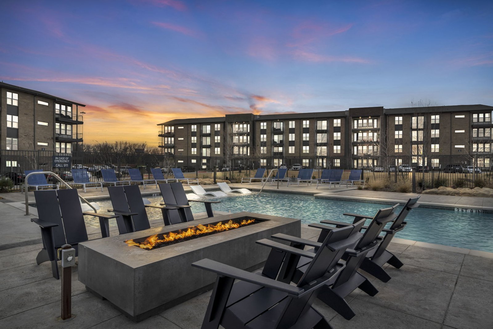 A poolside area with chairs and a fire pit in front of a building. at Axis Grand Crossing