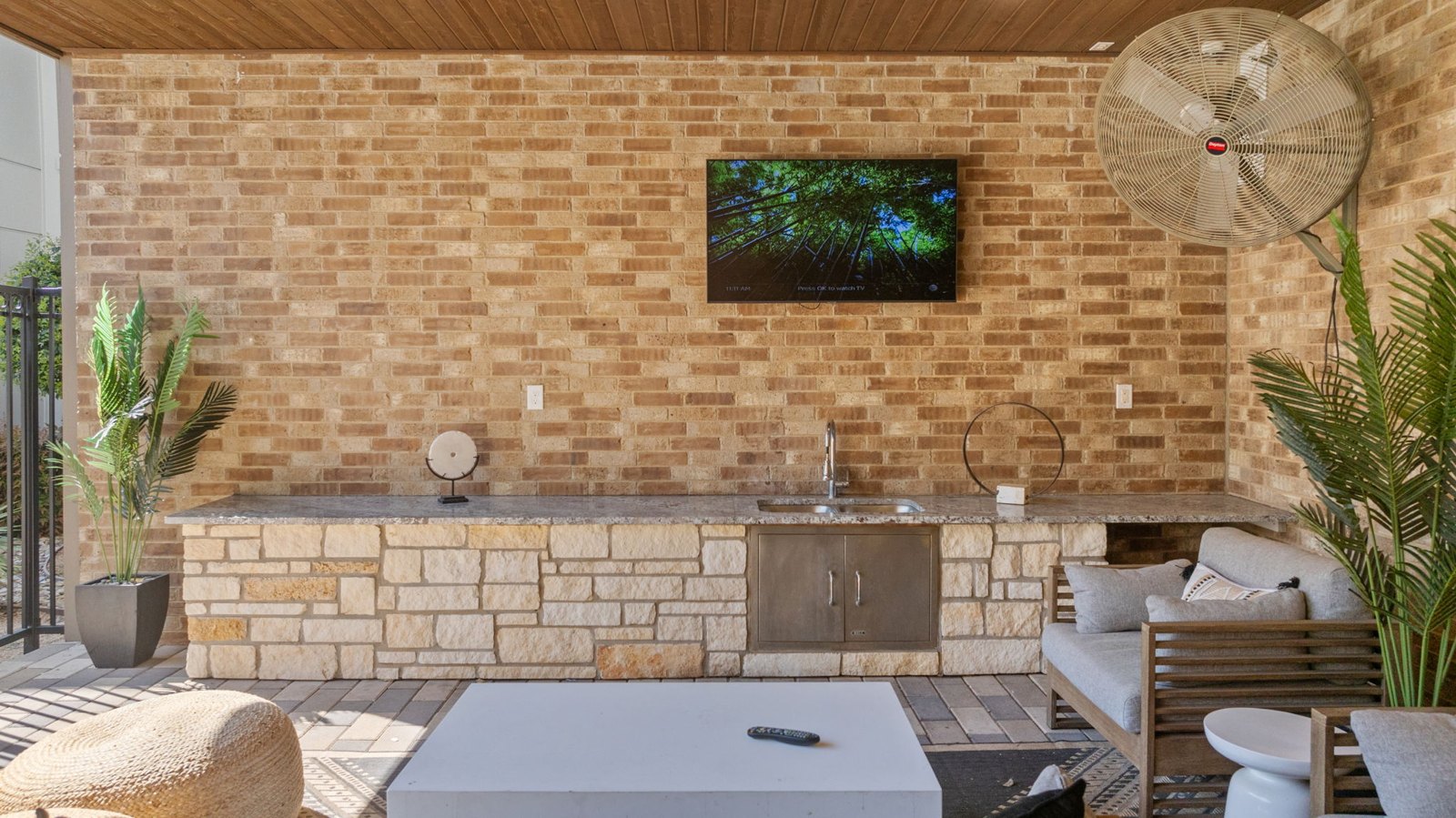 A modern outdoor living space with a brick wall and a television mounted above a fireplace. at Axis at Watters Creek
