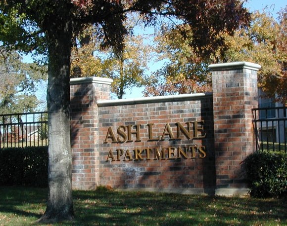 A sign for Ash Lane Apartments is displayed on a brick wall. at Ash Lane Apartment Homes