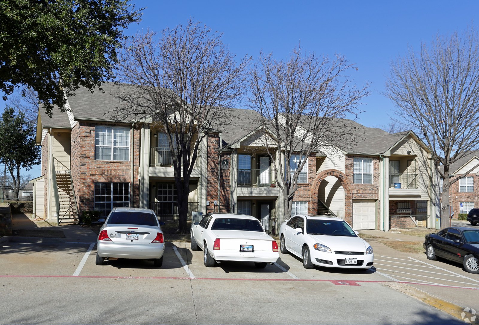 A white car is parked in front of a brick building. at Ash Lane Apartment Homes