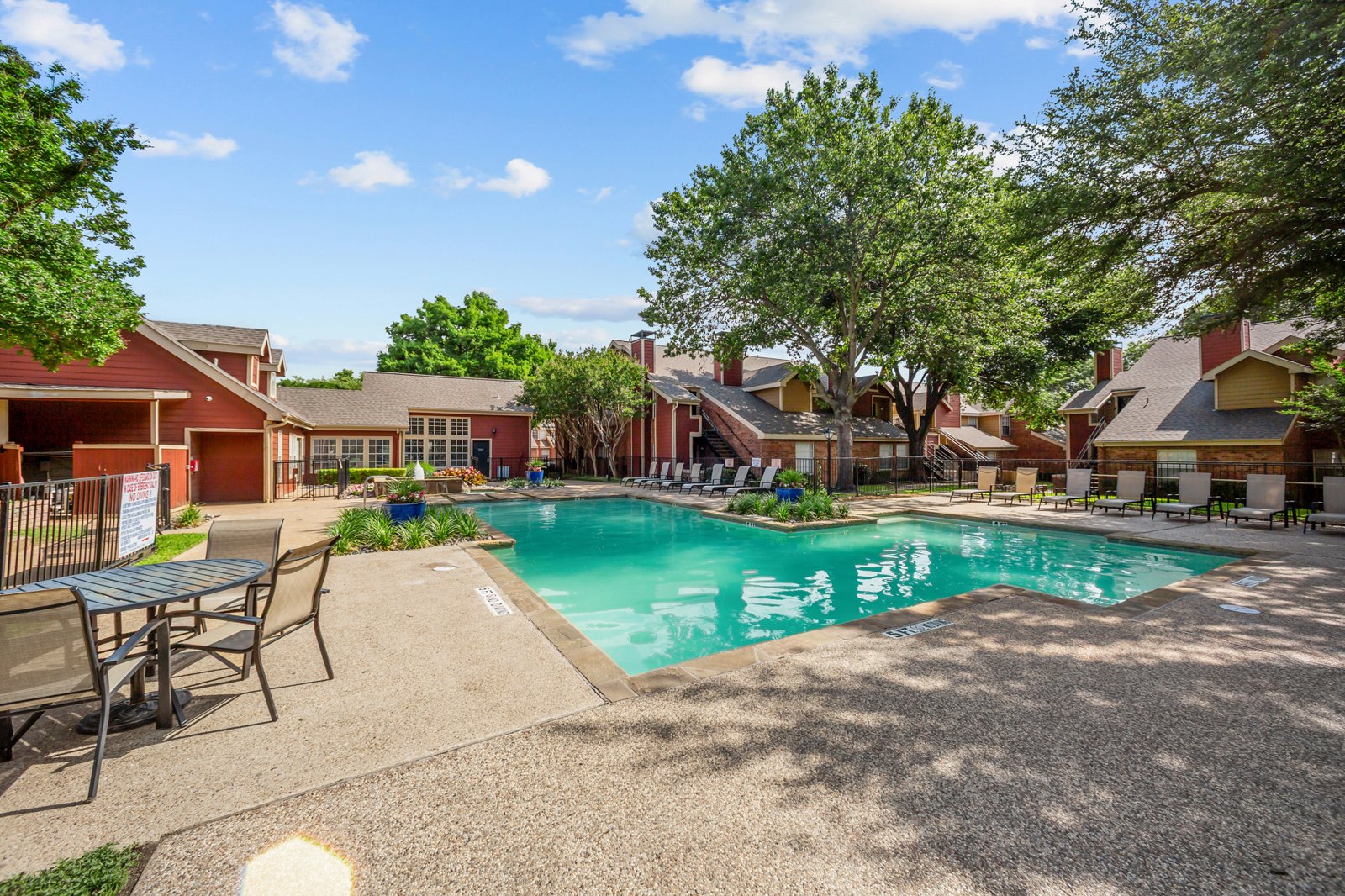 A pool surrounded by chairs and trees in a sunny day. at Bravo Apartment Living