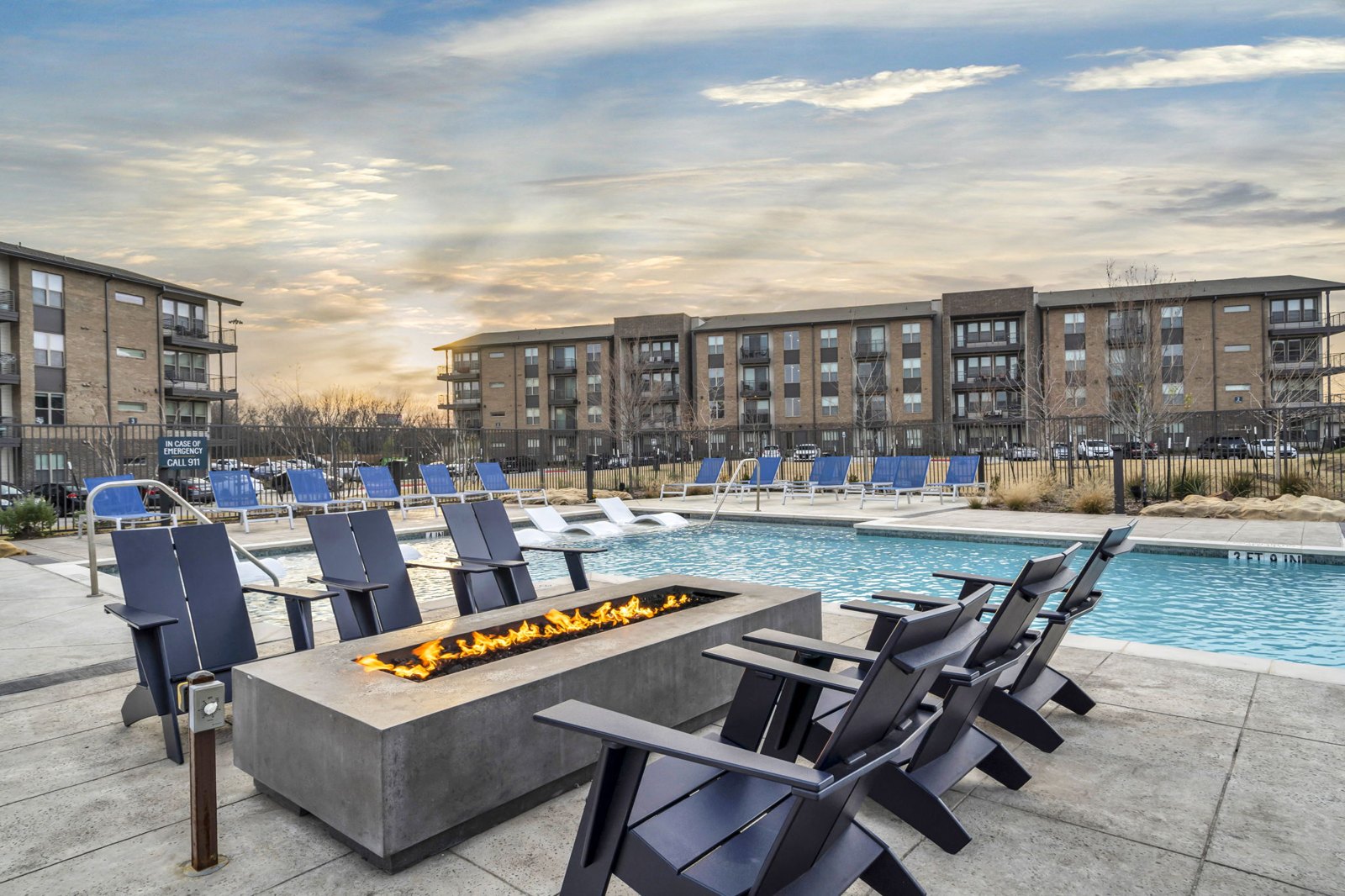 A fire pit sits in the middle of a pool surrounded by chairs. at Axis Grand Crossing