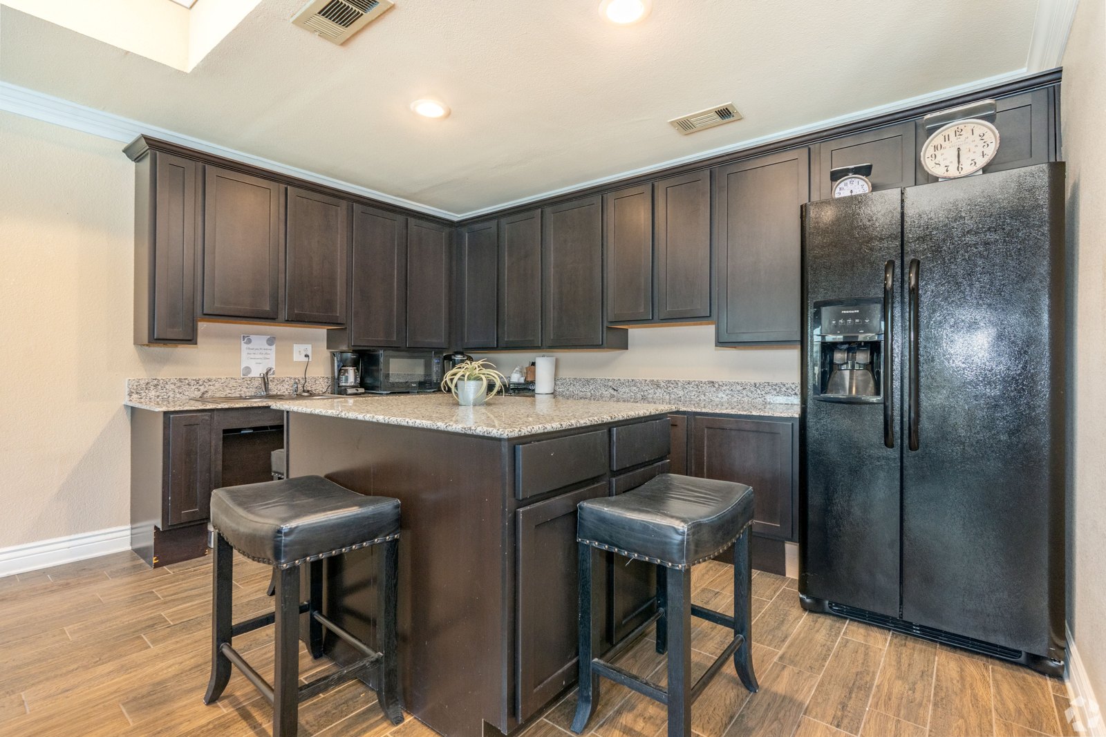 A kitchen with a black refrigerator and bar stools. at Ash Lane Apartment Homes